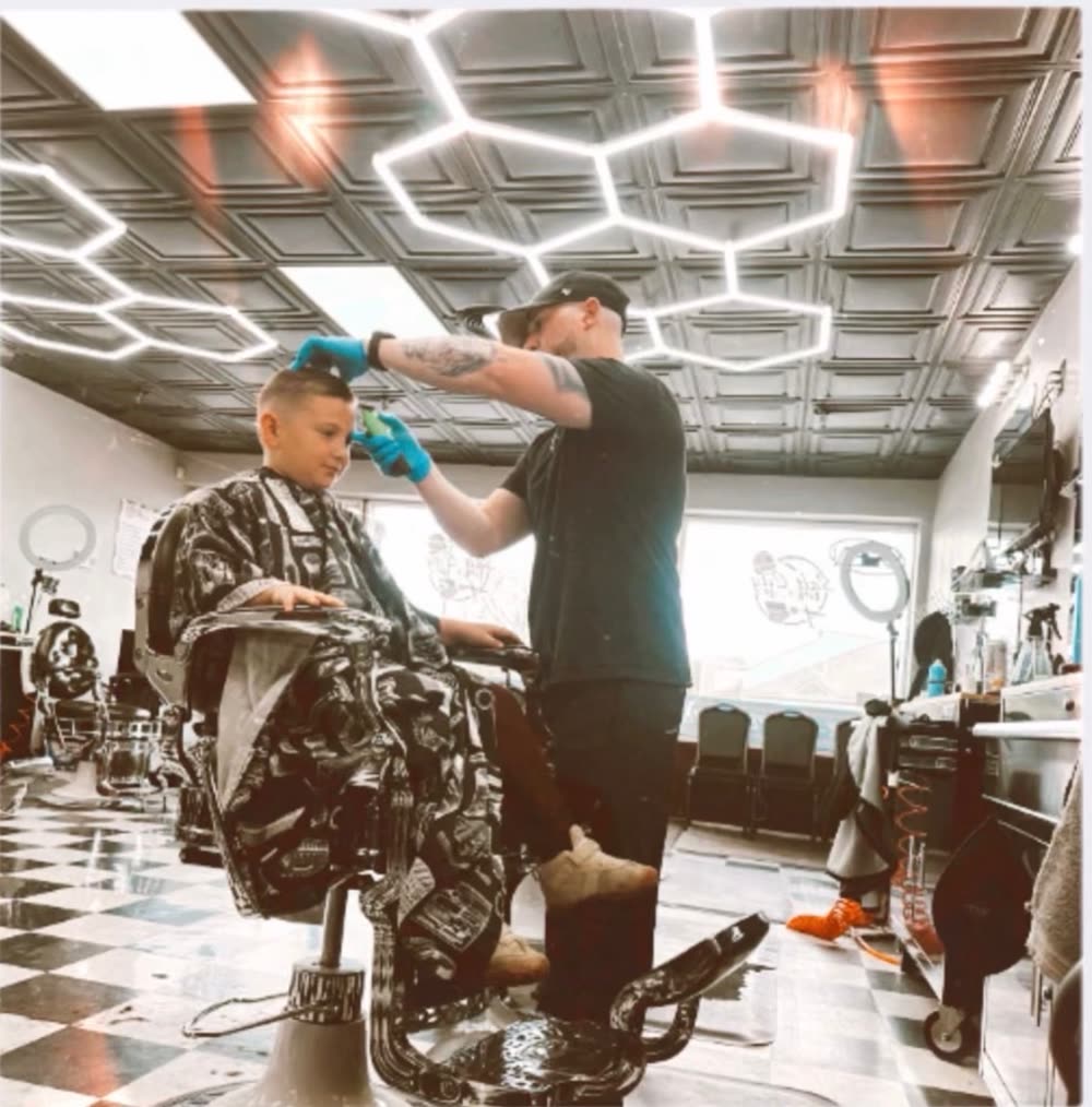 Barber giving a kids haircut under the hex lights at Salt City Barber Shop